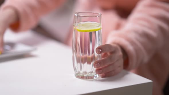 Closeup Water with Female Hand Putting Lemon Inside Taking Away Glass in Slow Motion alt