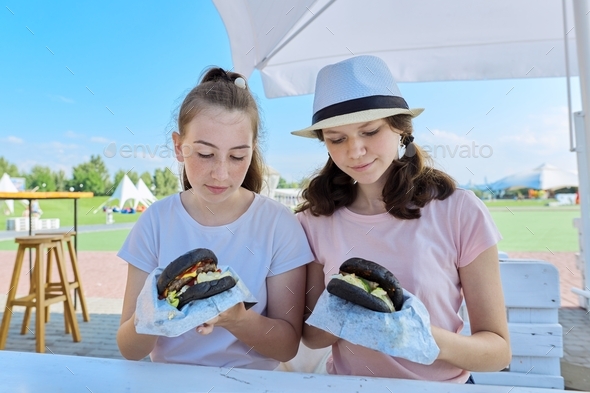 Teens two girls friends eating black burgers fast food, street food