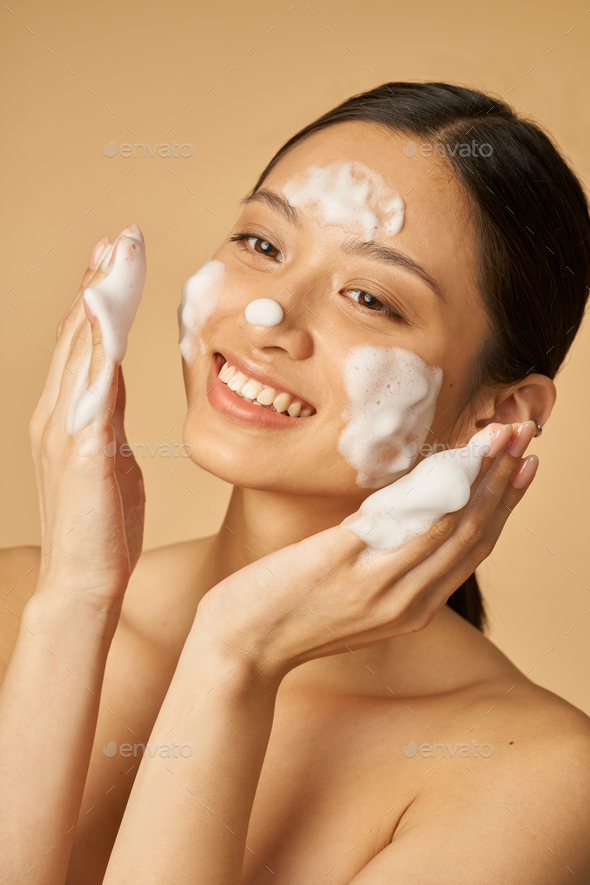 Beauty portrait of joyful young woman smiling while applying gentle foam facial cleanser isolated