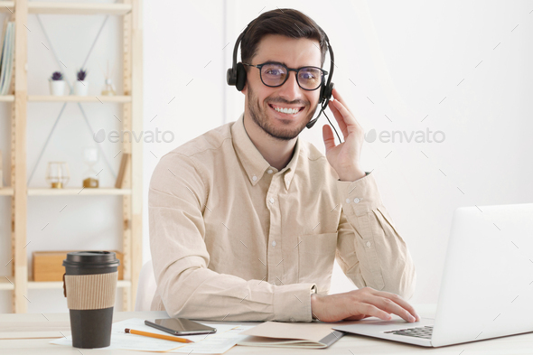 Young man from customer service supporting client via voice call, smiling happily at camera