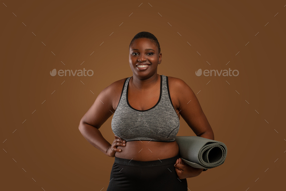 Chubby black woman holding yoga mat at studio Stock Photo by