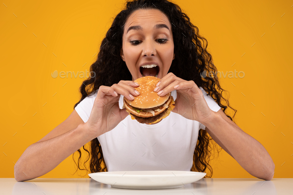 Happy Latin Lady Holding Burger Biting Sandwich At Studio