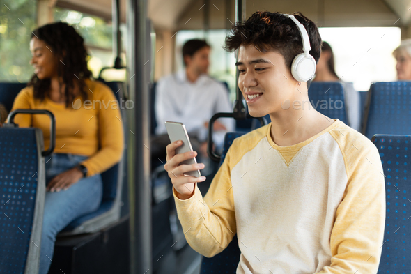 Happy Asian guy using smartphone and headphones in bus