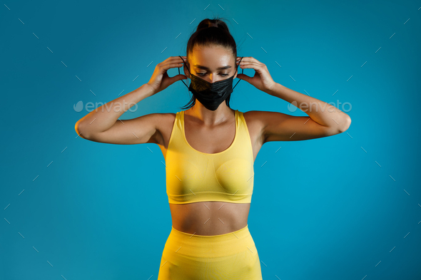 Sporty Woman Putting On Face Mask Standing On Blue Background