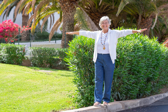 Playful senior woman walks on the curb with her arms outstretched to keep balance