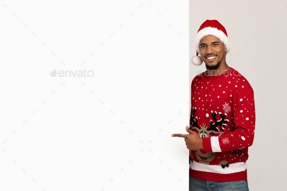 Happy black guy Santa Claus pointing at empty advertising board