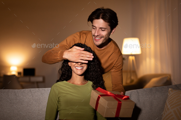 Loving Husband Giving Gift To Wife Covering Eyes At Home