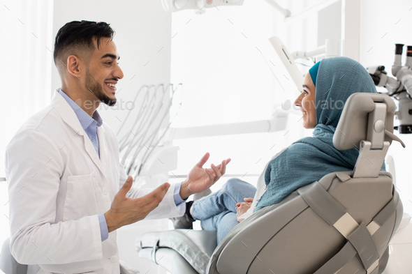 Handsome arab male dentist talking with muslim female patient at dental ...