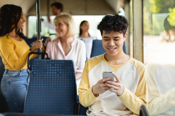 Happy Asian guy using cell phone in bus