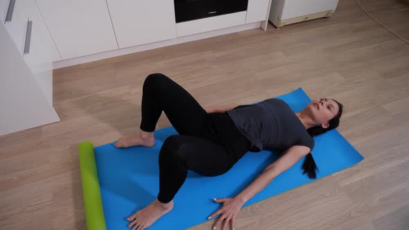 Sports Brunette Girl Performs Body Lifting Exercise Lying on a Blue Yoga Mat