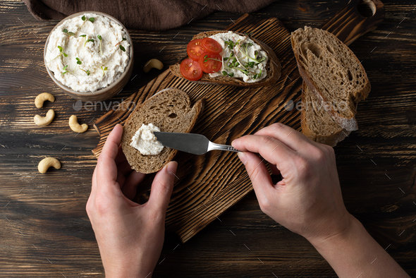 Female hands spreading vegan cashew cream cheese on a slice of bread.