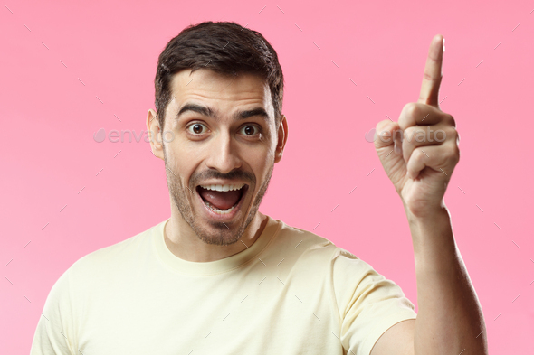 Attractive cheerful man keeps finger pointed upwards showing something above