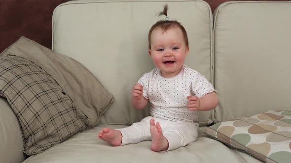 Funny Baby Sitting on Sofa Waving Hands and Smiling