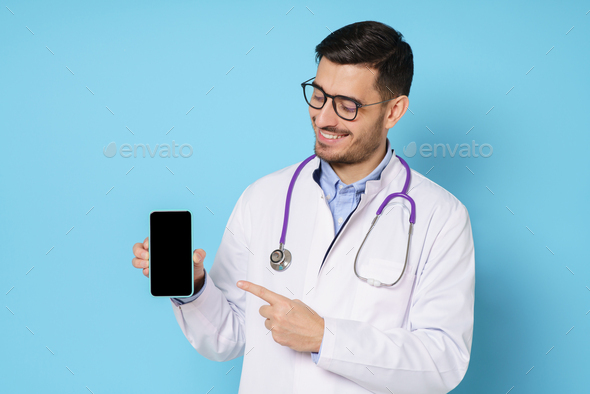 Young medic in white robe and glasses, showing commercial offer on blank phone screen