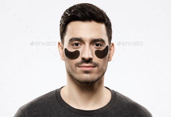Young man with black gel patches attached under eyes, willing to hide skin defects