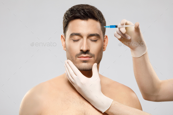 Young shirtless man receiving beauty injection in forehead to remove wrinkles