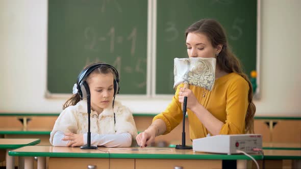 Young Girl and Teacher Using Headphones and Microphone in the Classroom alt
