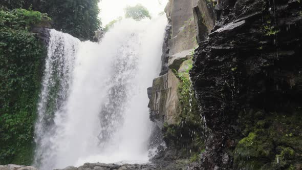 A Large Waterfall Surrounded By Jungle and Rocky Ledges with Water Drops Filmed in the Daytime