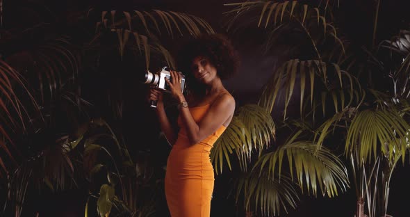 Woman With Afro Hair In Orange Dress Using Vintage 8Mm Camera alt