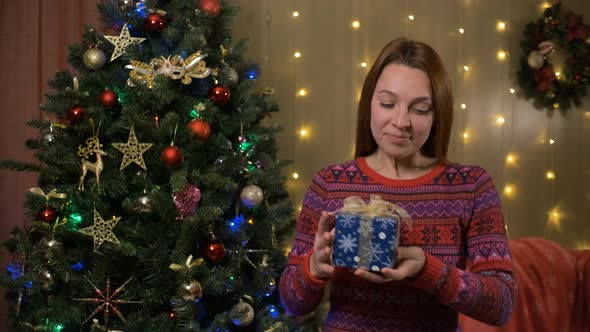 Young Beautiful Woman Shakes Box with Christmas Gift
