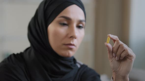 Young Female Thoughtful Patient Arabian Islamic Girl in Hijab Hold Yellow Medicine Capsule Vitamin alt