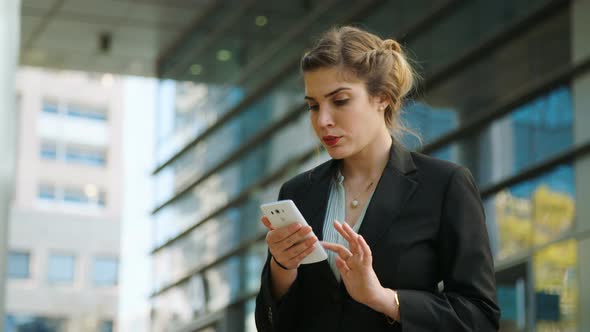 Young business woman walking on the street talking on her mobile phone alt