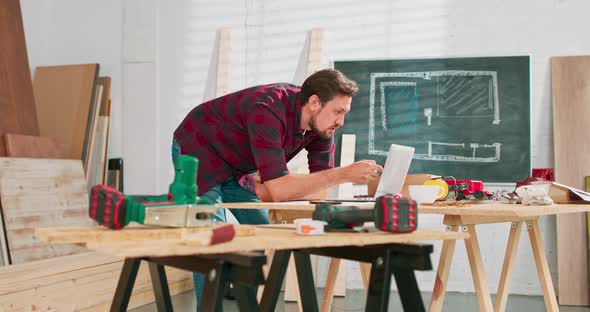 Portrait of Modern Young Bearded Man Speaking By Phone with Client Smiling and Making Notes in alt