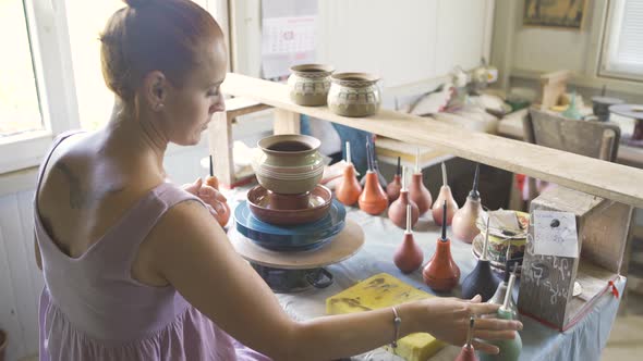 Female Potter Painting and Glazing Clay Pot with Precision Using Special Tools alt
