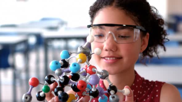 Attentive schoolgirl experimenting molecule model in laboratory alt
