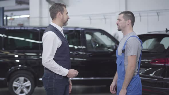 Side View of Two Caucasian Men Standing in Auto Repair Shop and Talking. Successful Businessman alt