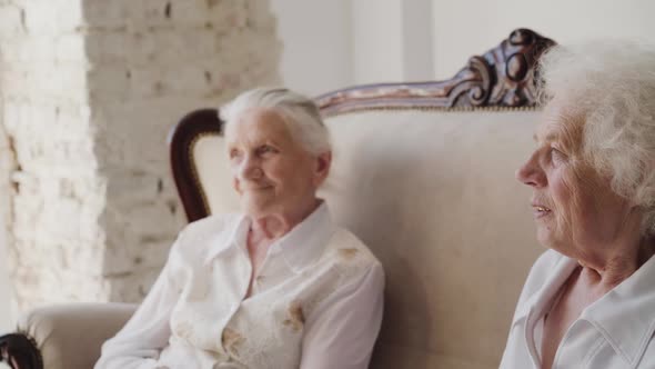 Two Cute Grandmothers Sitting on a Sofa and Talking Among Themselves in Room alt