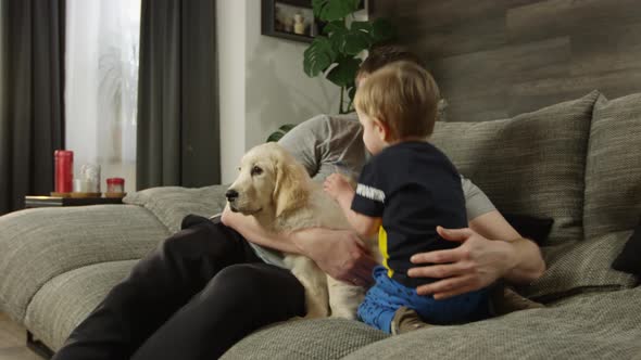 A Child a Golden Retriever and a Father Resting on a Sofa in the House alt