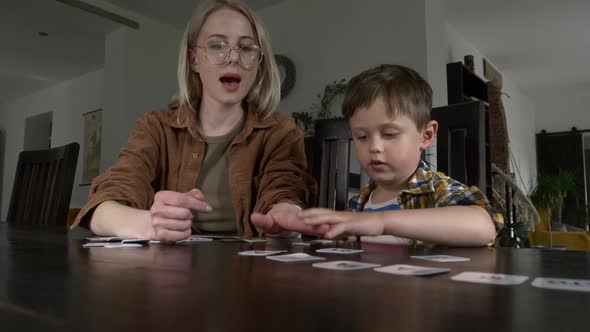 Mom teaches her son how to say the words on the cards at home at the table