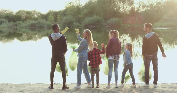 Activists which Standing on the Lake's Bank with Filled Rubbish Bags and Giving High Five alt