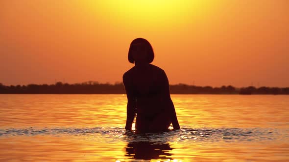Silhouette of Woman at Sunset Raises Hands Up and Creating Splashes of Water. Slow Motion alt