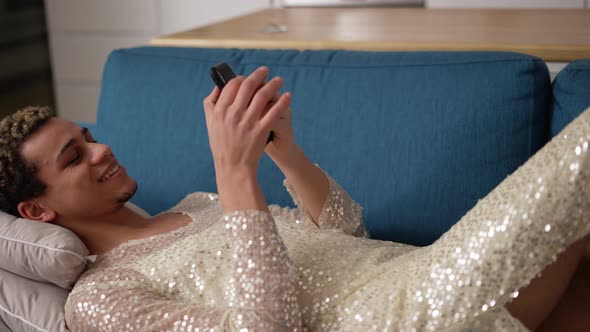 Cheerful Guy in Fancy Dress Using Mobile Phone Laying on Sofa alt