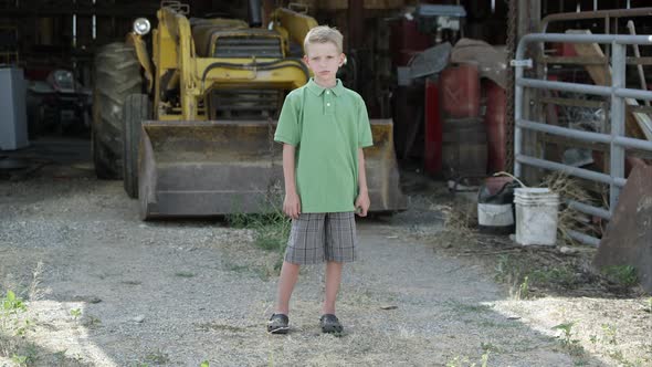 Slow motion of boy with cleft lip standing in front of tractor. alt