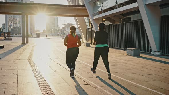 Follow Shot of Two Active Overweight African American Female Friends Running in City in Evening Back alt