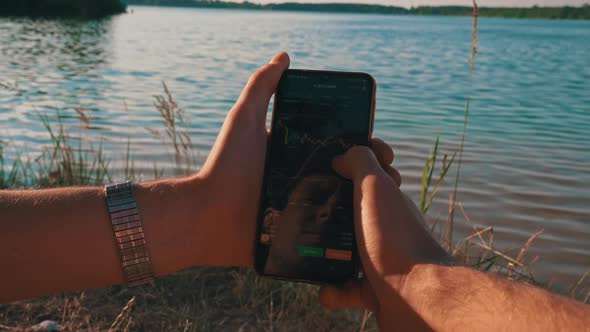 Hands of a Man with a Smartphone and Cryptocurrency Near the River in Nature alt