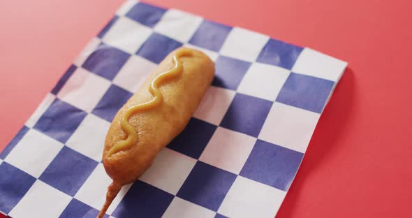 Video of corn dog with mustard on a red surface alt