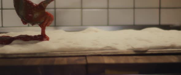 Tomato sauce being spread over a fresh pizza dough. Close up, super slow motion. alt