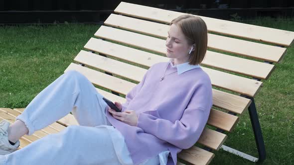 Melancholic Lady Student Listens to Music Sitting on Bench alt