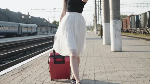 Confident Lady in Dress Walks at Camera with Red Suitcase on Railway Platform alt