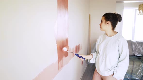 Young Woman in White Pullover Colours Wall in Brown Lazily