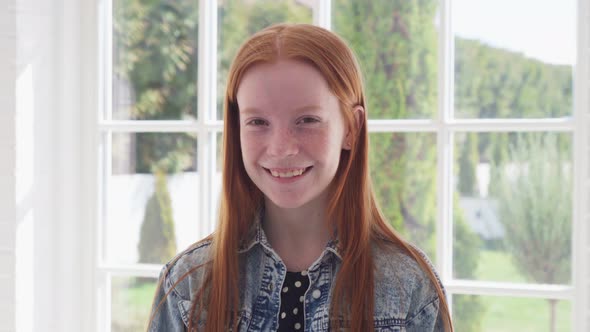 Happy Ginger Girl with Freckles Smiling Against White Window
