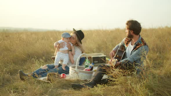 Man Playing Guitar for Family During Picnic