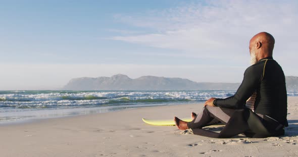 Senior african american man sitting with a surfboard at the beach alt