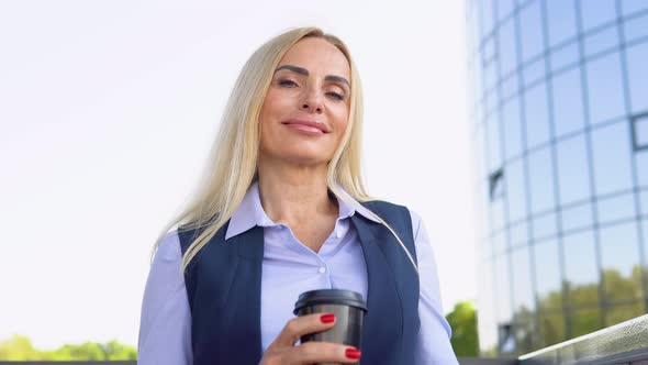 Senior Businesswoman Standing Outside a Modern Corporate Building with Coffee Cup alt