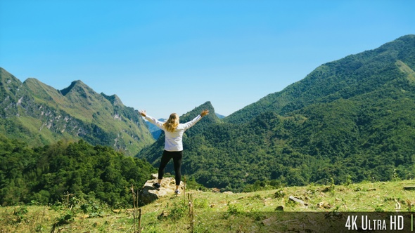 4K Rear View of Tourist Woman Walking to Mountain Summit with Beautiful Scenic View and Raising Arms alt