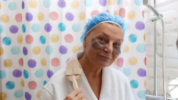 Aged Cheerful Woman in Shower Cap and Eye Pads Singing Song Holding Body Brush alt